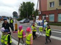 Kolejna grupa przedszkolna podczas przemarszu ulicami Zambrowa. Dzieci idą z plakatami promującymi zdrowy styl życia. Rejon skrzyżowania zabezpiecza funkcjonariusz WRD, w tle radiowóz policyjny.