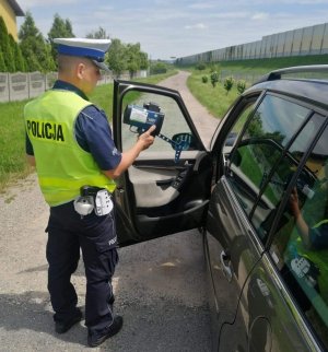 Umundurowany policjant ,,drogówki&quot; w ręku trzyma miernik prędkości, który wskazuje kierowcy zarejestrowaną prędkości pojazdu.